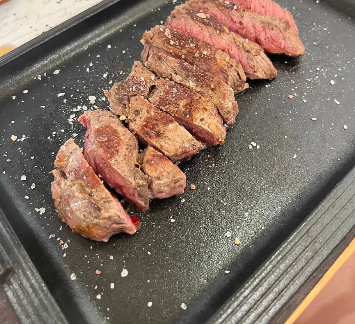 Tagliata di manzo alla griglia, cotta al sangue, servita a fette con sale grosso su piastra nera